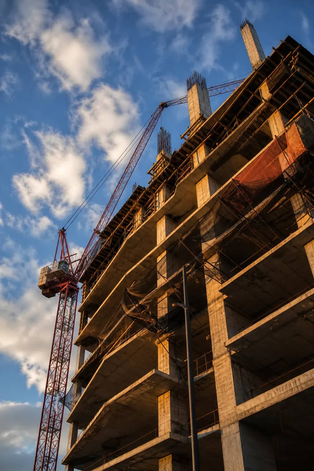 Reinforced concrete high-rise under construction with exposed column dowels and a tower crane against a blue sky